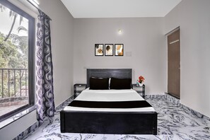 Un dormitorio con cama, mesita de noche, ventana con cortinas y tres cuadros enmarcados en la pared.