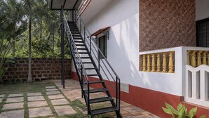 Una escalera conduce a un balcón con un muro de ladrillo, un patio con baldosas y una pequeña zona ajardinada.