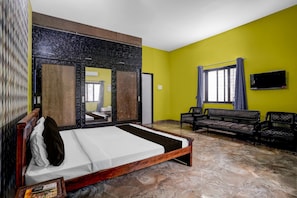 Una habitación de hotel con cama, sofá, televisión y ventana con cortinas.