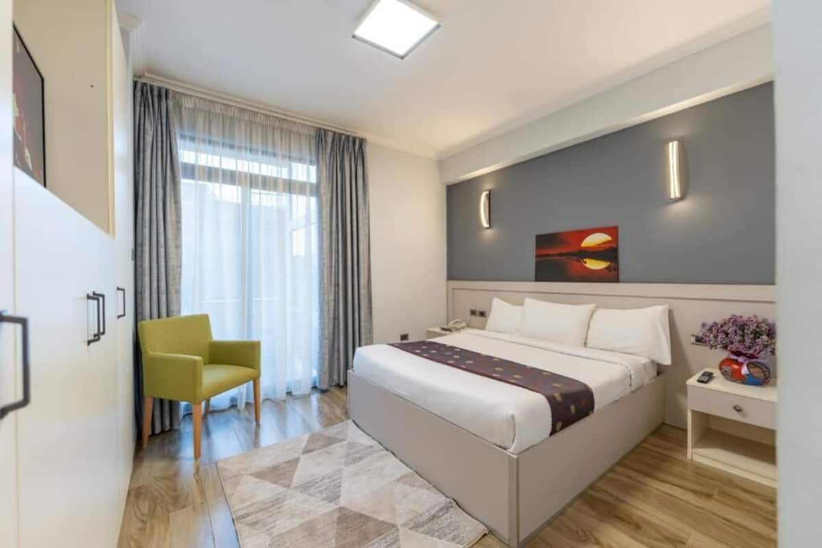 A modern hotel room with a bed, a chair, a nightstand, and a painting on the wall.