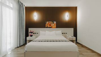 A modern hotel room with a large bed, bedside tables, a nightstand, a painting on the wall, and a window with curtains.