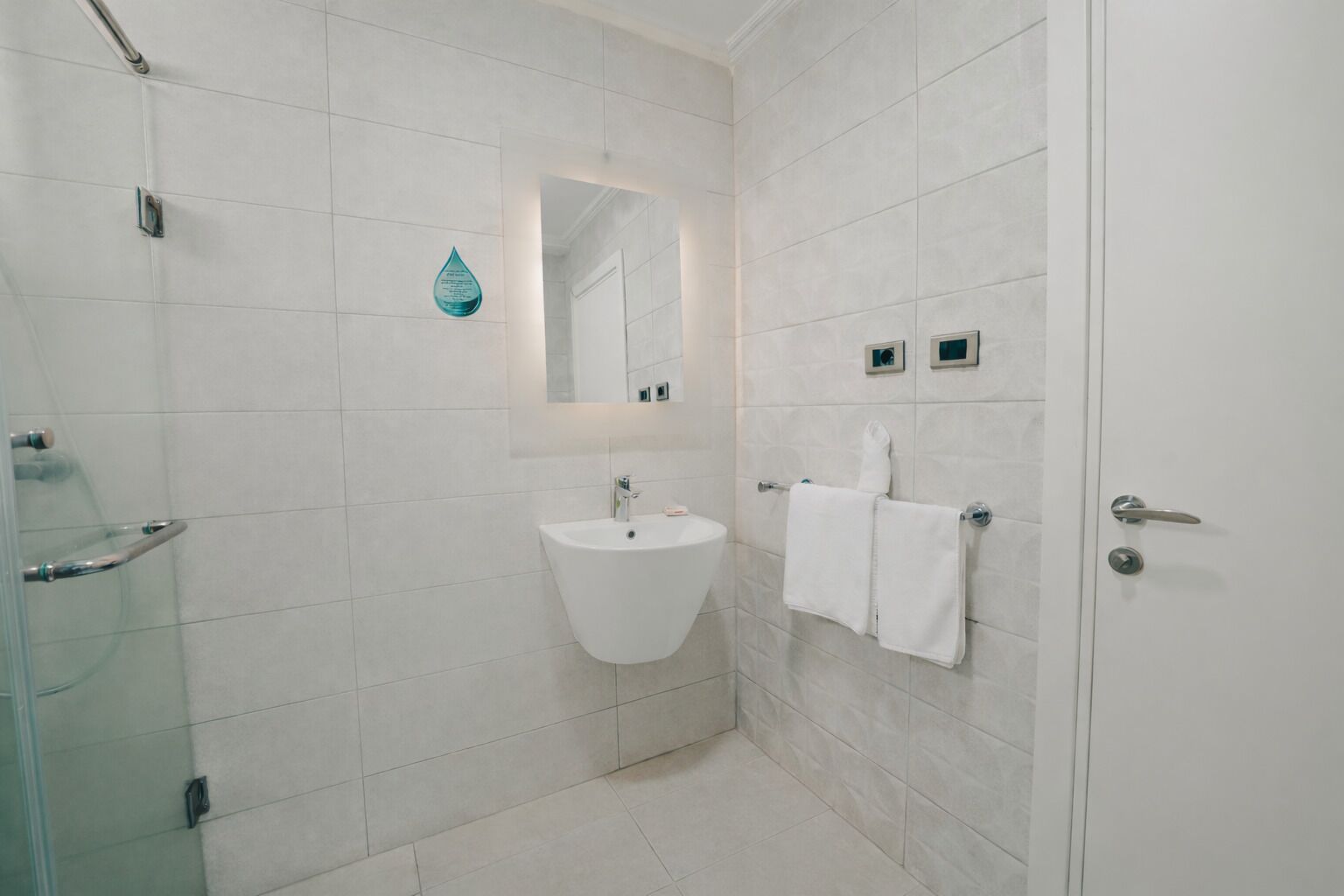 Un bagno moderno con un lavandino bianco, una cabina doccia in vetro e un portascopevoli.