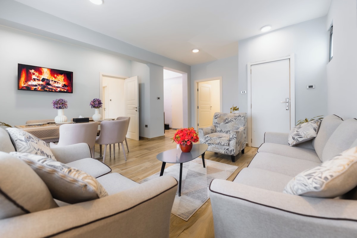 A modern living room with a flat-screen TV, a dining area with a table and chairs, and a seating area with sofas.