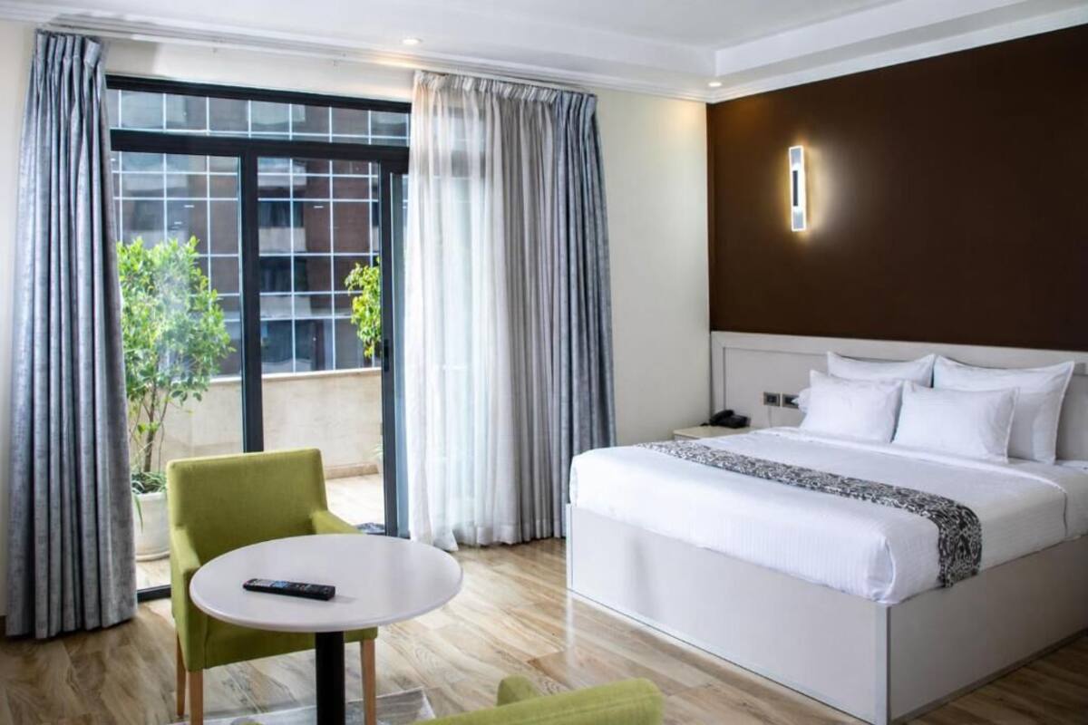 A hotel room with a bed, a round table, a chair, and a view through a large window.