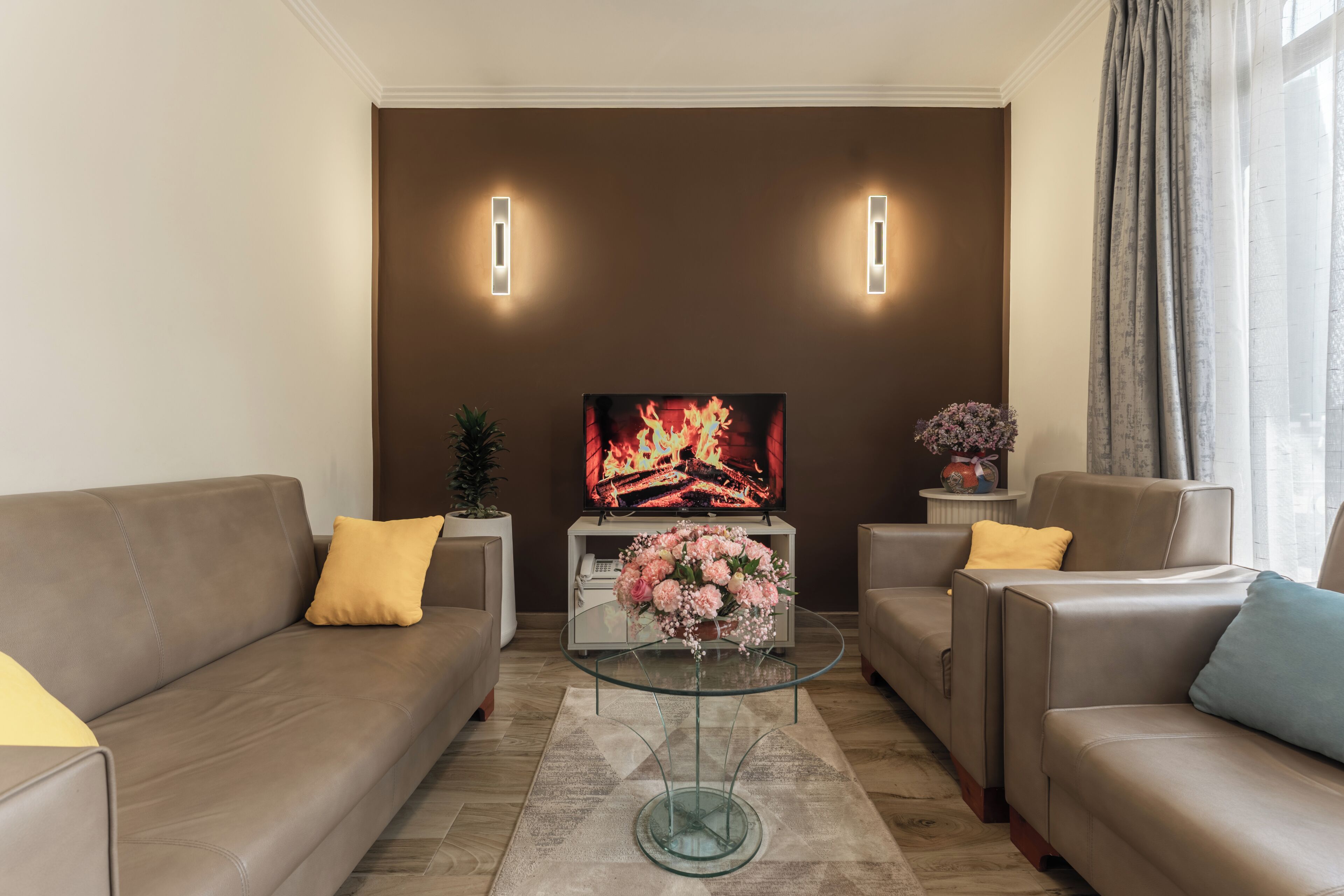 A living room with a sofa, a glass coffee table, a TV, and wall-mounted lights.