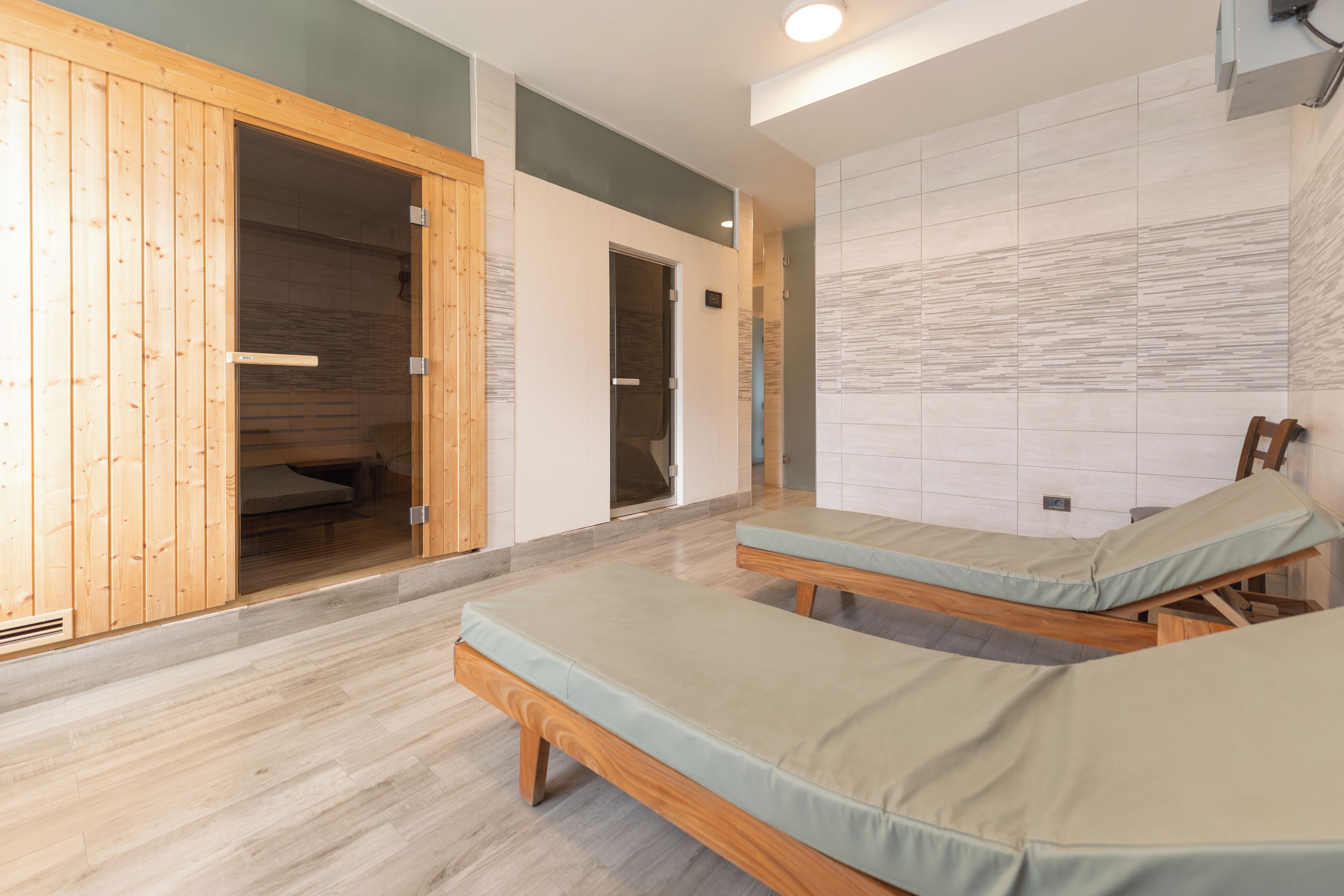 A room with two wooden beds, a sauna, and a tiled wall.