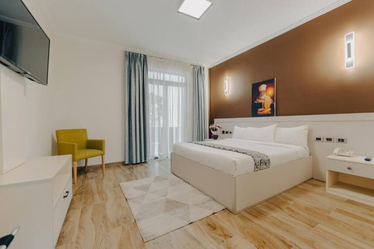 A hotel room with a bed, a desk, a chair, a TV, and a painting on the wall.