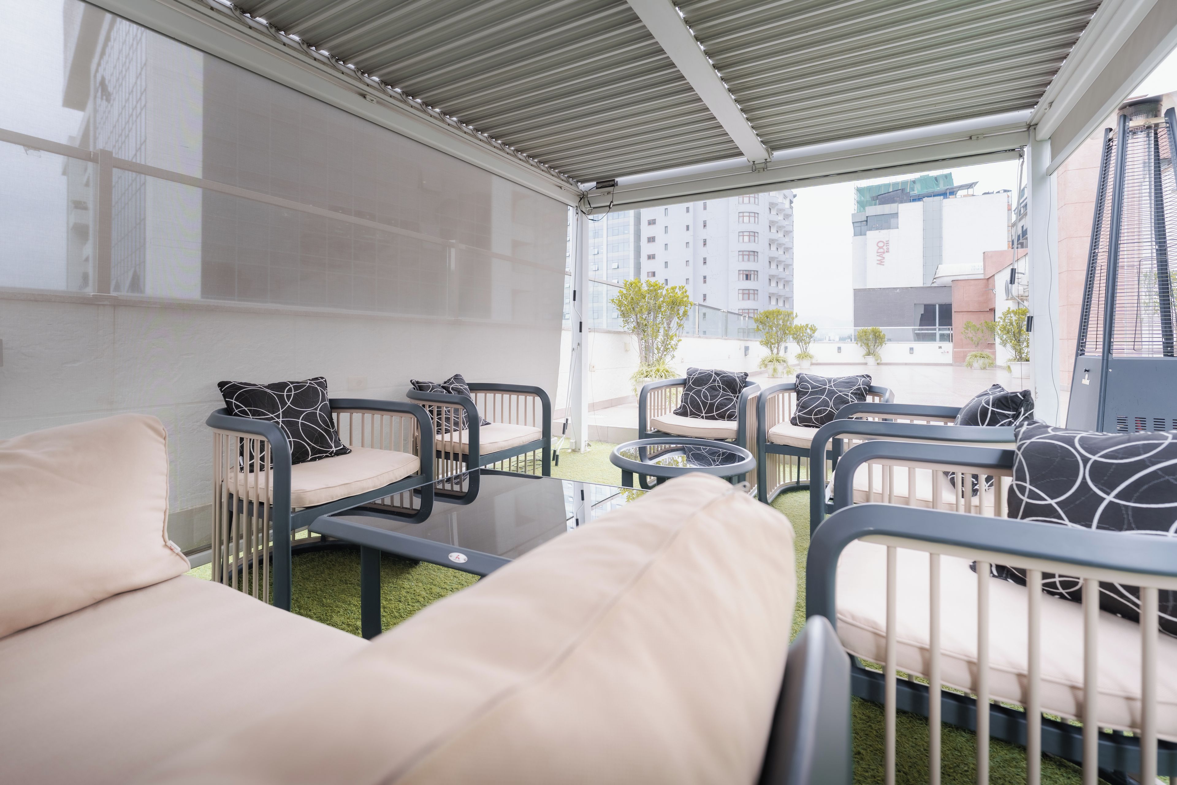 A modern outdoor seating area with a glass table, cushioned chairs, and a view of a cityscape.