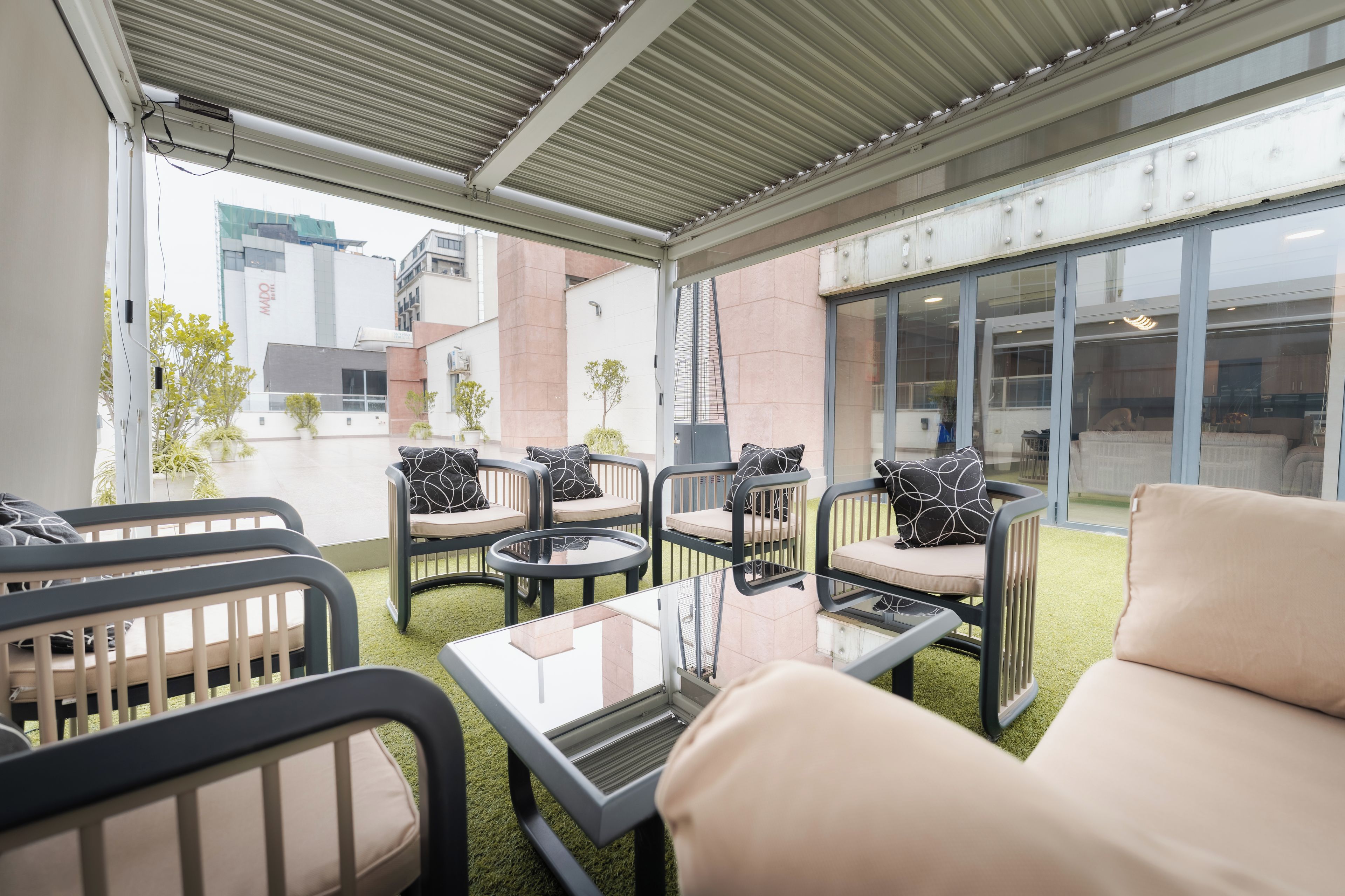 An outdoor seating area with multiple chairs and tables, a glass door leading to a covered patio, and a view of a building with a sign.