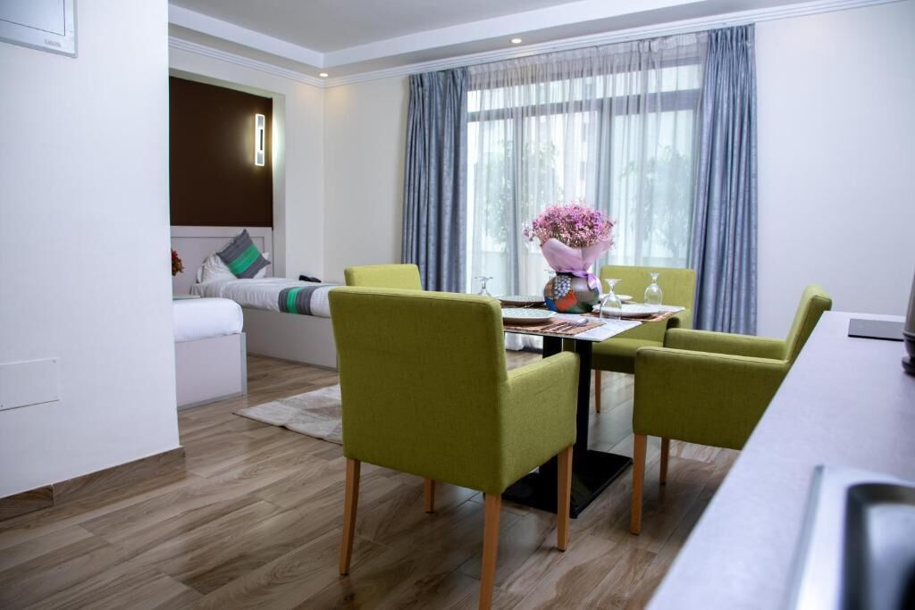 A modern hotel room with a dining area, a sofa, and a large window with curtains.
