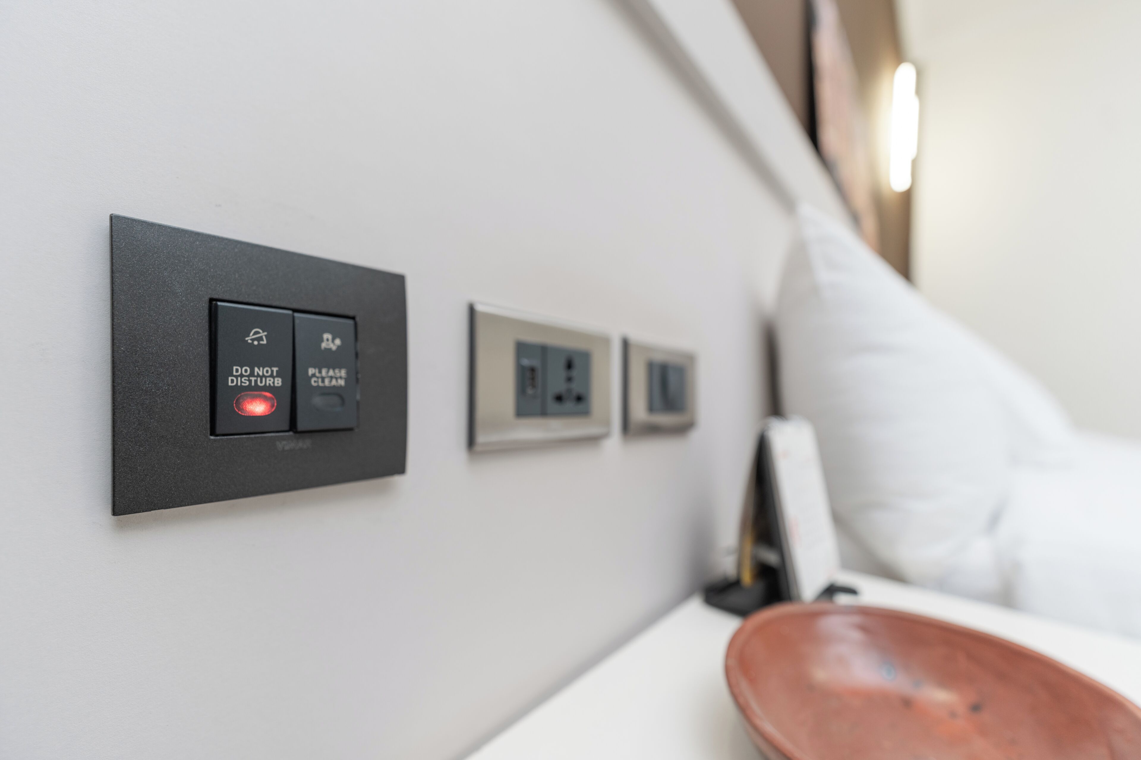 A wall-mounted control panel with a 'DO NOT DISTURB' button and a 'PLEASE CLEAN' button, along with two electrical outlets.