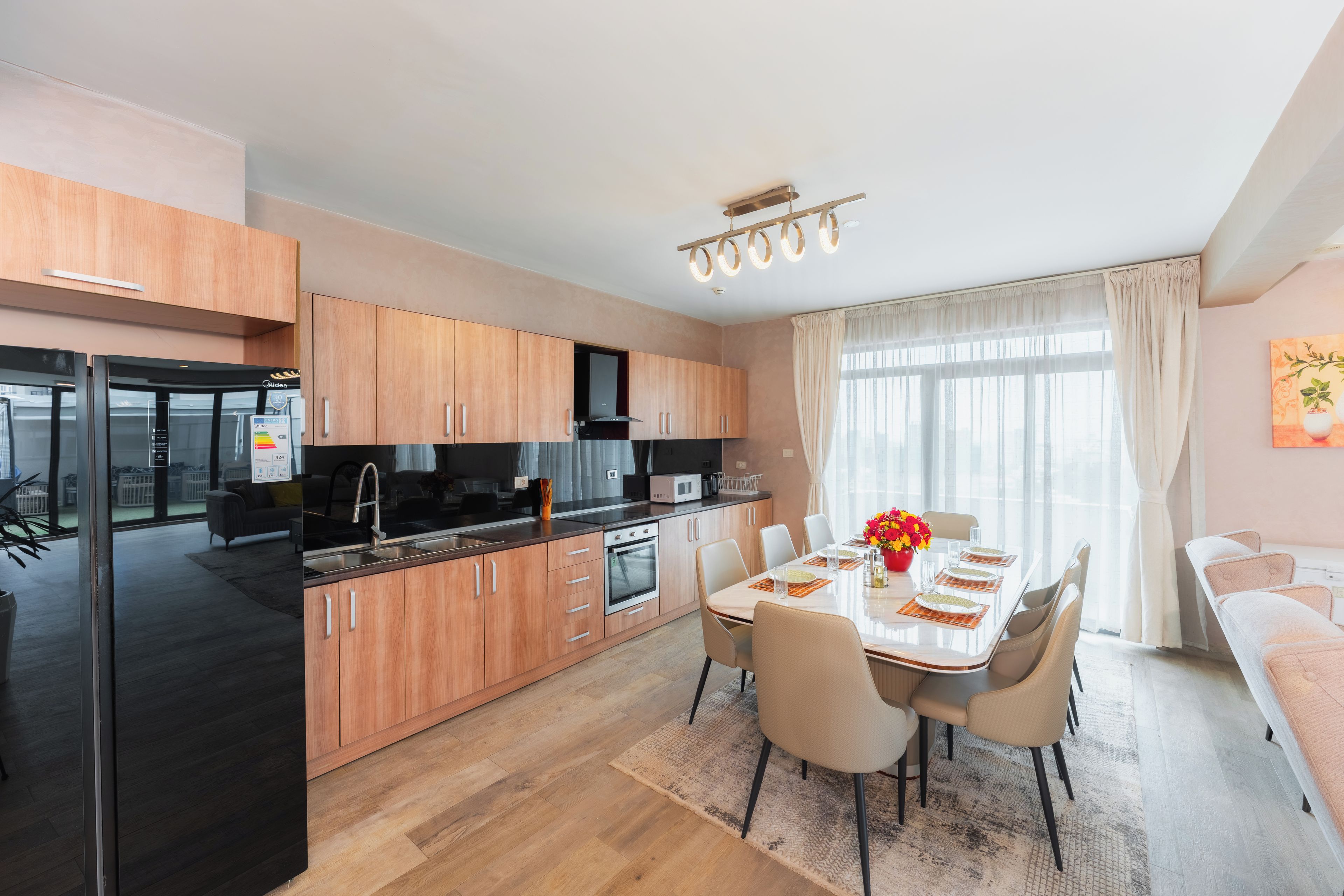 Una cocina moderna con armarios de madera, un comedor con una mesa preparada para cuatro personas, y vistas de la ciudad a través de amplios ventanales.