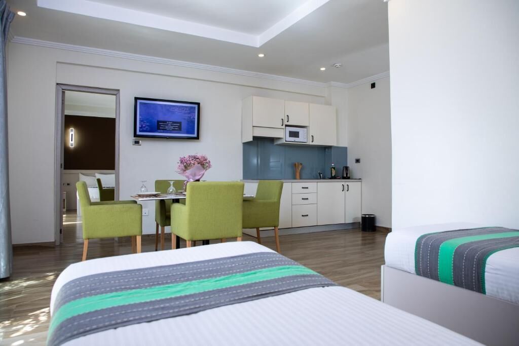 Una habitación de hotel con cama, escritorio con sillas, kitchenette y televisor.