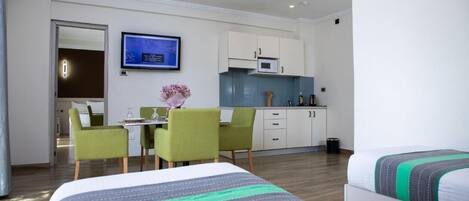 Una habitación de hotel con cama, escritorio con sillas, kitchenette y televisor.