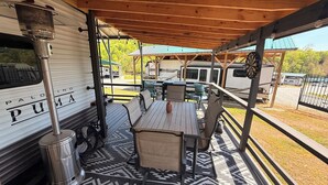 A covered outdoor area with a table and chairs, a trash can, and a grill. - Wake&Lake at Norris Landing Marina-Waterfront RV Retreat with Deck + Slip Option (Tazewell)