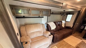 A compact RV interior with a sofa, a small table, and a window. - Wake&Lake at Norris Landing Marina-Waterfront RV Retreat with Deck + Slip Option (Tazewell)