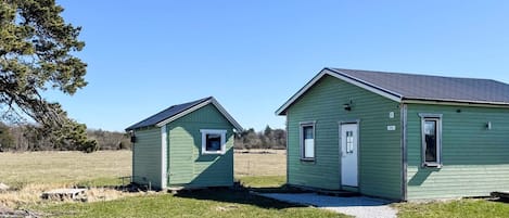Two small, single-story houses with green siding and white trim, connected by a gravel path.