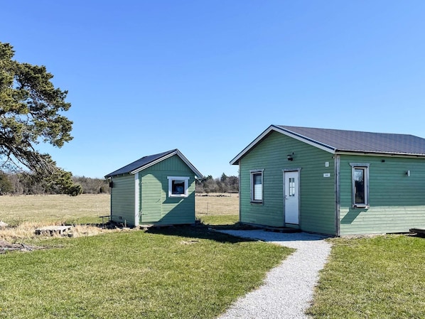 Two small, single-story houses with green siding and white trim, connected by a gravel path. - 4 Person Holiday Home in Hemse (Hemse)