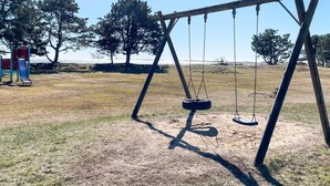 Une balançoire dans un parc, avec un toboggan et des arbres en arrière-plan.