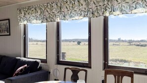 Une pièce avec vue sur un champ, une table recouverte d’une nappe à motifs et une fenêtre avec un rideau.