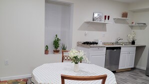 Un comedor con una mesa redonda, sillas, una planta en maceta y una cocina al fondo.