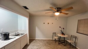 Cocina compacta con ventana, ventilador de techo, lavamanos y comedor con sillas y mesa.