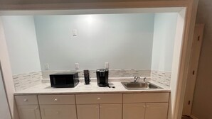 Una kitchenette pequeña con microondas, cafetera y lavabo.