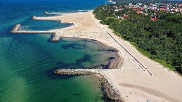 An aerial view of a coastal area with a beach, a pier, and a town in the background. - Two-story Holiday Homes With a Summer Pool (Postomino)