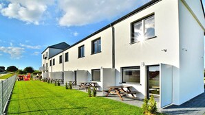 A modern building with multiple windows, a flat roof, and a well-maintained lawn with picnic tables. - Two-story Holiday Homes With a Summer Pool (Postomino)