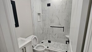 Moderni kylpyhuone, jossa on wc, pesuallas ja suihkutila.