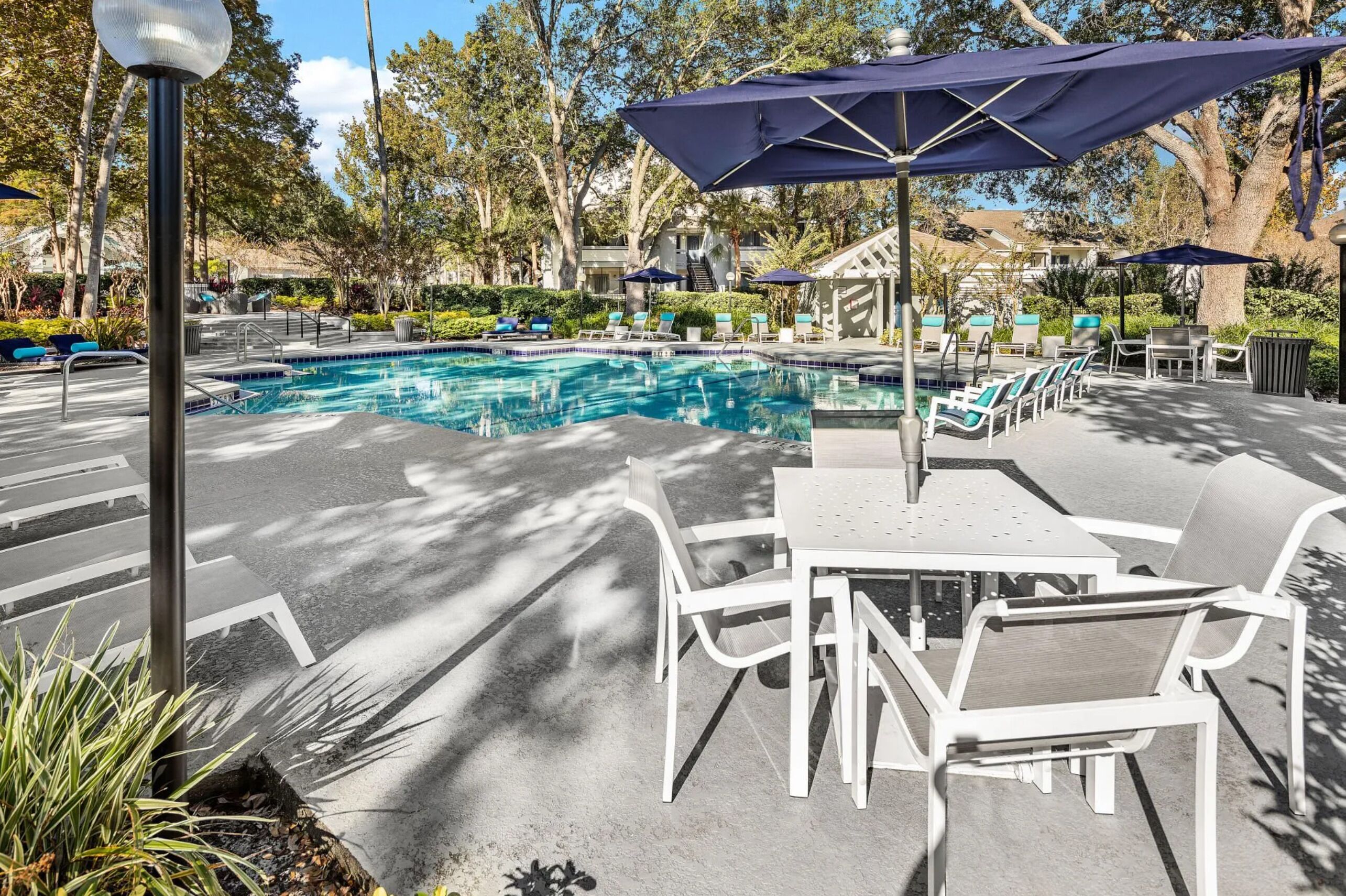 Zona de piscina con sillones de descanso, sombrillas y una mesa.