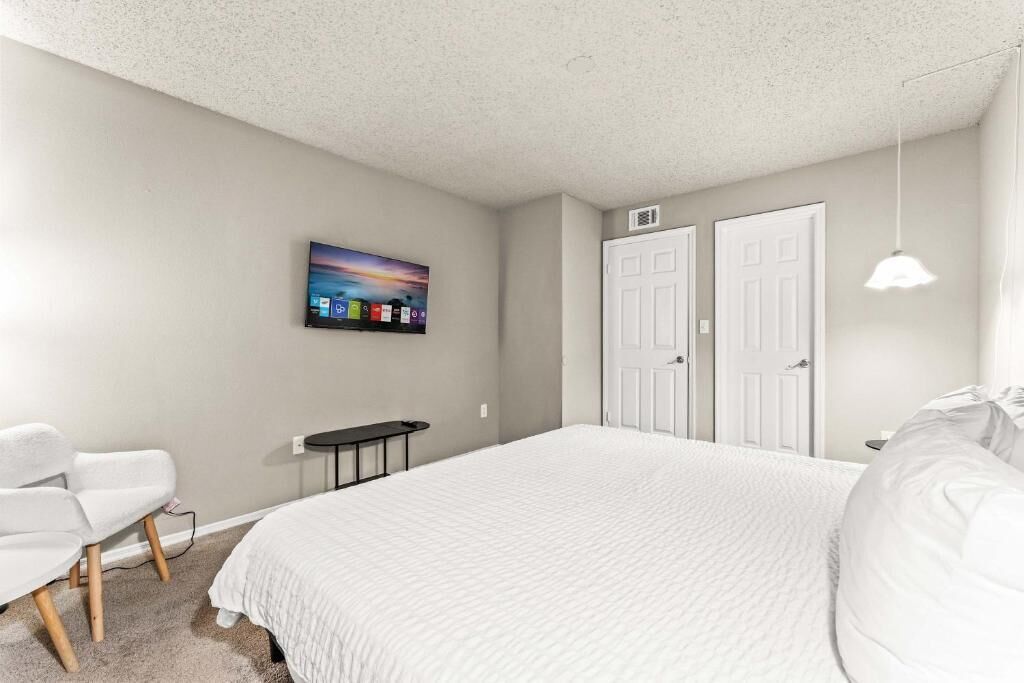 A bedroom with a bed, a desk, a chair, and a wall-mounted TV.