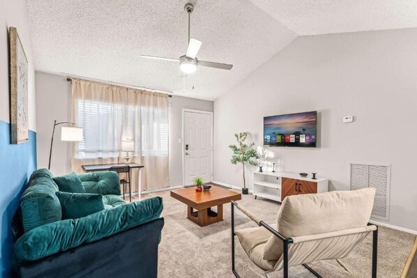 A living room with a sofa, armchair, coffee table, TV, and a ceiling fan. - Solara Apartments Spacious 2BR Apartment Sleeps 6 Pet-Friendly (Orlando)