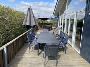 A deck with a table and chairs, a grill, and a large umbrella. - 4 Star Holiday Home in Borkop (Borkop)