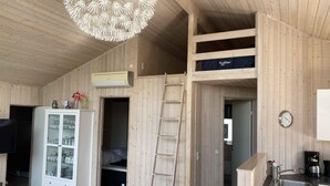 A wooden interior with a bunk bed, a white cabinet with glass doors, a ladder, a kitchen area with a sink, and a wall clock. - 4 Star Holiday Home in Borkop (Borkop)