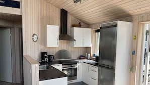A compact kitchen with white cabinets, a stainless steel refrigerator, a built-in oven, and a coffee maker. - 4 Star Holiday Home in Borkop (Borkop)