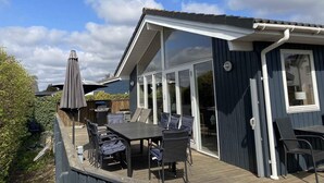 A deck with a table and chairs, a covered umbrella, and a sliding glass door leading to a room. - 4 Star Holiday Home in Borkop (Borkop)