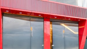 Una entrada moderna de edificio con dos puertas grandes, fachada roja y una escalera que conduce a la entrada.