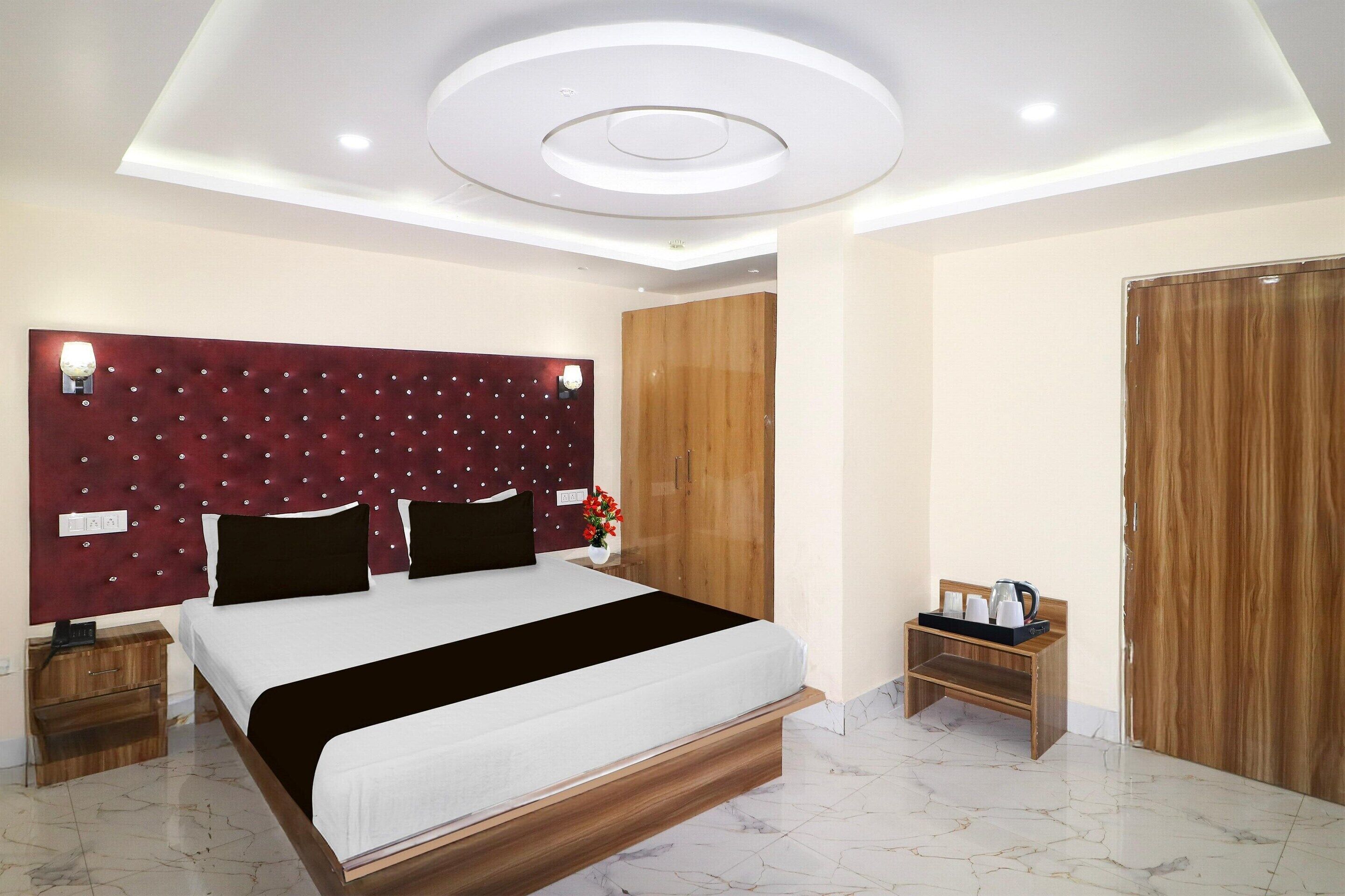 A modern hotel room with a large bed, a wooden headboard, a wooden wardrobe, a bedside table with a lamp, and a small wooden side table with a tray.