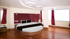 A modern bedroom with a curved bed, a round ceiling light fixture, and a large window with curtains. - Super Deluxe Room Bank More Dhanbad (Dhanbad)
