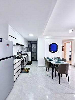 Eine moderne Küche mit weißen Schränken, einem eingebauten Backofen und einem Essbereich mit Tisch für vier Personen.