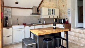 A kitchen with white cabinets, a wooden island, bar stools, a stainless steel sink, and a microwave.