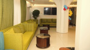A modern living room with a yellow sofa, a green sofa, a round wooden coffee table, and a white pillar with balloons. - Sylhet Regency Ltd. (Sylhet)