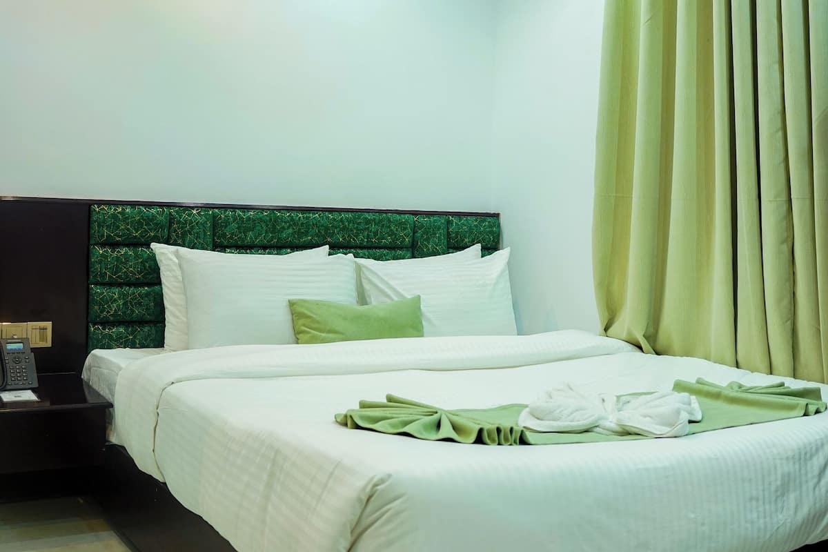 A modern hotel room with a large bed, a headboard with a green pattern, a bedside table with a phone, and a curtain on the window.