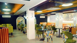 A restaurant with green and orange seating, tables, and a mural on the wall. - Sylhet Regency Ltd. (Sylhet)