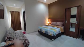 A bedroom with a bed, a sofa, a bedside table, a lamp, and a mirror.