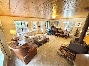 A cozy living room with a sofa, armchair, coffee table, dining table, chairs, and a wood-burning stove. - Hamilton branch Creekside Cabin in the Trees (Westwood)