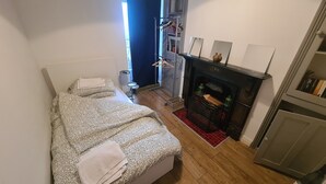 Una habitación pequeña con cama, cómoda, chimenea y armario.