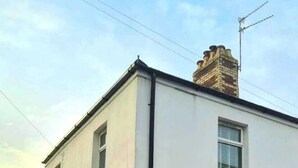 Un edificio residencial de dos pisos con fachada blanca, una chimenea de ladrillo y un coche estacionado en la entrada.