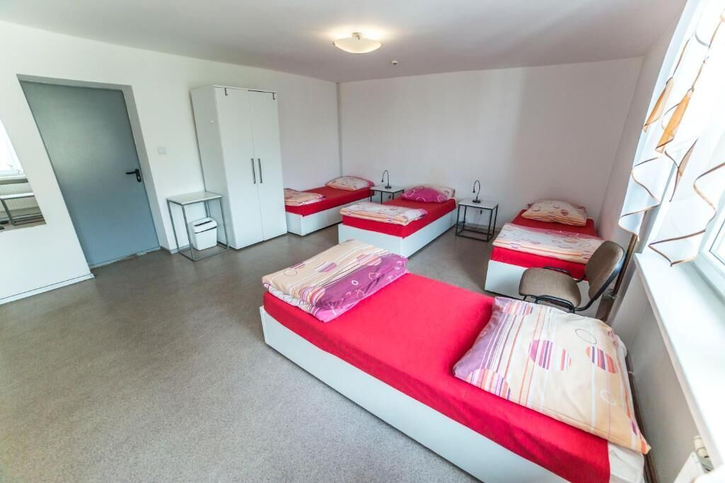 A room with three beds, a wardrobe, a small table, and a window with curtains.